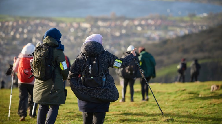 Walkers at the top of a cliff looking down at the view of a town and resevoir